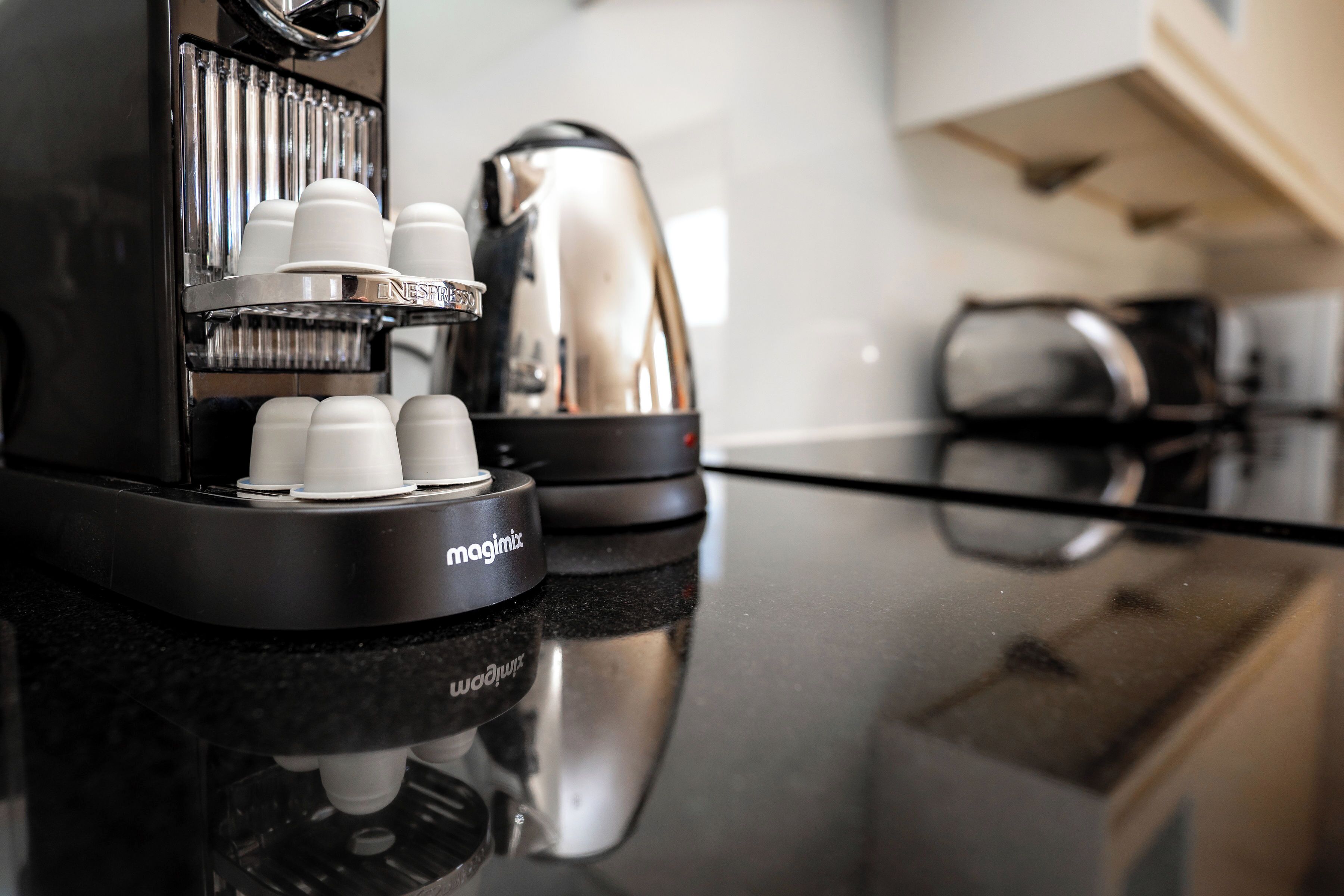 Una macchina per caffè con diverse tazze e un bollitore su una superficie riflettente.