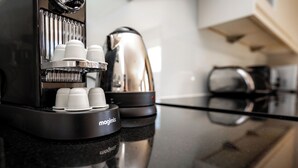 Una cafetera con varias tazas y una tetera sobre una superficie reflectante.