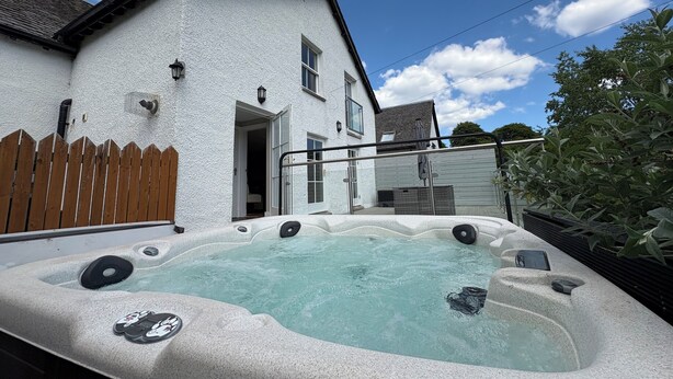 Un jacuzzi frente a una casa blanca con valla de madera y cielo despejado.