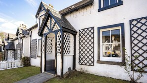 Una casa tradicional blanca con estructura de madera negra, un pequeño jardín y una valla de piquetes blancos.