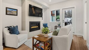Un salon moderne doté d’une cheminée, d’un téléviseur fixé au mur et offrant une vue sur l’extérieur.