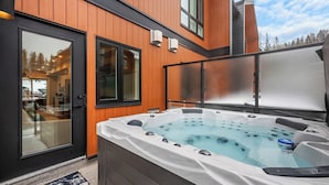 Un bain à remous installé à l’extérieur, avec des murs en bois et une porte en verre.