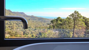Vista desde una ventana con paisaje de montaña, árboles y cielo despejado.