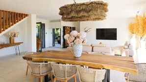 Amplia sala de estar con una gran mesa de comedor de madera, sillas de mimbre y una lámpara colgante de paja.