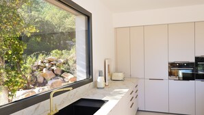 Una cocina moderna con un amplio ventanal, armarios blancos y un lavamanos negro.