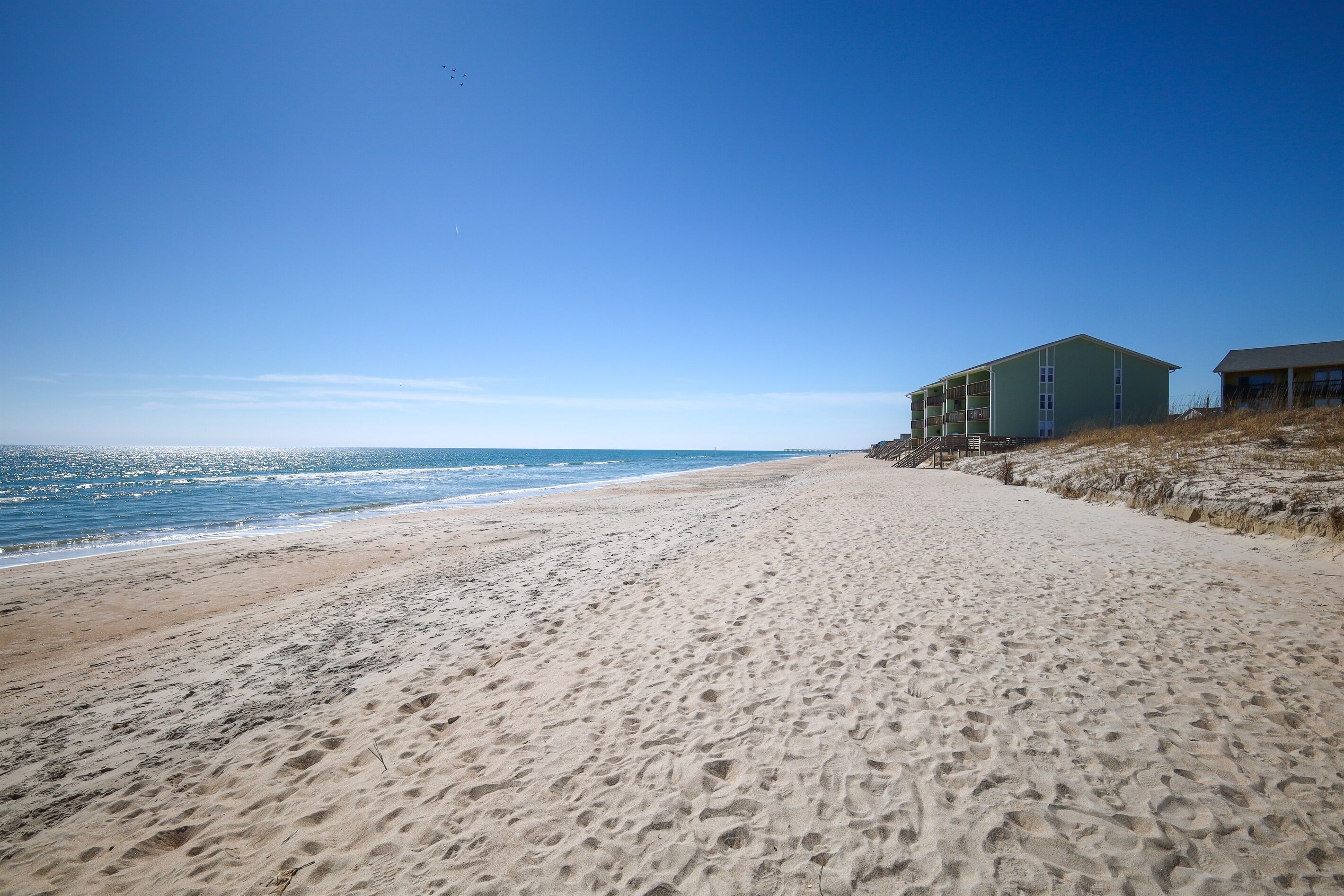 A beach with a building that has multiple floors and balconies.