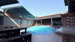 An outdoor pool area with stone flooring, picnic tables, and a barbecue grill. - Hotel Villa Jardín (Matamoros)