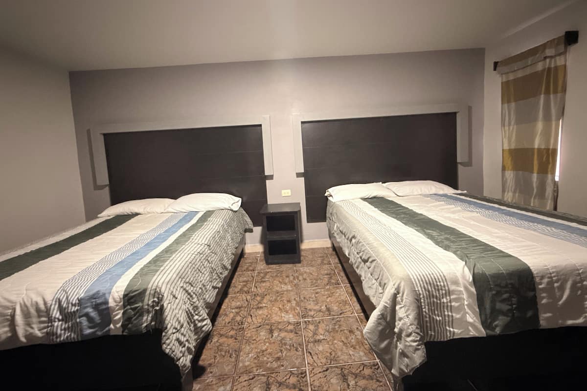 Habitación doble con dos camas, una mesita de noche pequeña y suelo de baldosas.