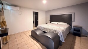 A bedroom with a bed, a bench, a wardrobe, and a small bedside table. - Hotel Villa Jardín (Matamoros)