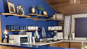 Een keuken met een blauwe betegelde achterwand, houten planken, een bar met witte stoelen en een keukenbord.