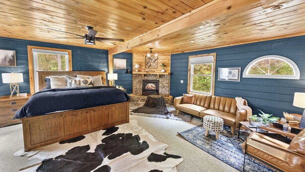 Een gezellige slaapkamer in chaletstijl met een houten plafond, een stenen openhaard, een groot bed, een leren bank en een kleden van runderhuid.