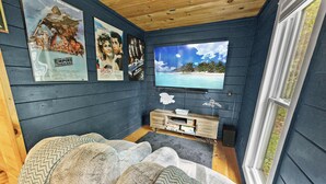 Een gezellige kamer met een grote televisie, houten plafond en een raam.