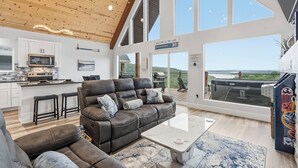 A modern interior with a leather sofa, a kitchen, and large windows offering a view of the outdoors. - New Lake-View Luxe Cabin w/ Pvt Hot Tub, 3/2 Sleeps 8! EV Charger, Branson, SDC! (Branson)