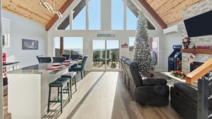 A spacious living area with a large island, a fireplace, and a view of the outdoors. - New Lake-View Luxe Cabin w/ Pvt Hot Tub, 3/2 Sleeps 8! EV Charger, Branson, SDC! (Branson)