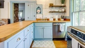 Una cocina con armarios azul claro, encimera de madera, horno empotrado y ventana con vista a árboles.