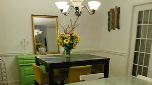 Un coin repas avec une table à plateau en verre, des chaises blanches, un buffet vert et un vase rempli de tournesols.