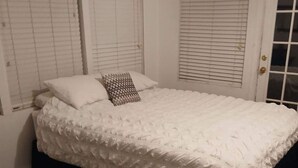 Une chambre à coucher avec un grand lit, du linge de lit blanc et un coussin à motifs.