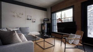 A modern living room with a sofa, a coffee table, a fireplace, and a large window with a view of trees.