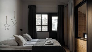 A bedroom with a bed, two bedside tables, a window with curtains, and a view of trees outside.