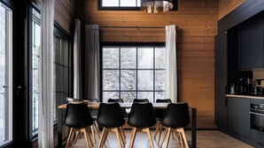 A modern kitchen with a wooden interior, a dining area with a wooden table and black chairs, and large windows with curtains.