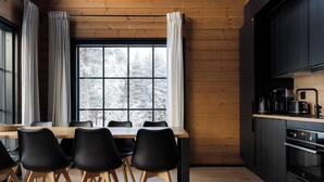 A modern kitchen with a wooden table and chairs, a large window with curtains, and a built-in oven.