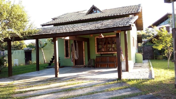 A covered outdoor area with a tiled roof, wooden benches, and a small table. - Located 300 meters from the beach, the house faces east and is surrounded by grass. (Florianópolis)