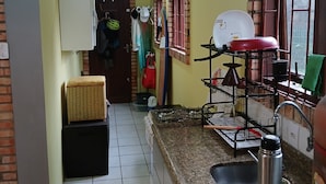 A compact kitchen with a gas stove, sink, and a small refrigerator. There is a window with bars and a basket on the counter. - Located 300 meters from the beach, the house faces east and is surrounded by grass. (Florianópolis)