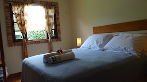 A hotel room with a bed, curtains, a nightstand, and a lamp. - Located 300 meters from the beach, the house faces east and is surrounded by grass. (Florianópolis)
