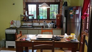 A kitchen with a dining area, a refrigerator, a stove, and a ceiling fan. - Located 300 meters from the beach, the house faces east and is surrounded by grass. (Florianópolis)