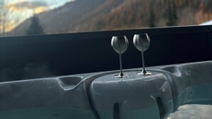 Uma banheira de hidromassagem com duas taças de vinho na borda, com vista para uma paisagem montanhosa.