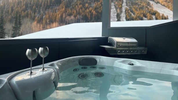 Uma banheira de hidromassagem com duas taças de vinho em uma varanda com vista para uma paisagem montanhosa.