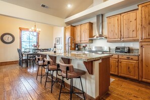 A kitchen with wooden cabinets, a granite countertop, a bar area with stools, a sink, and a window with natural light. - Lodges 1193 (Mammoth Lakes)