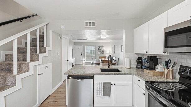 A modern kitchen with white cabinetry, granite countertops, a stainless steel dishwasher, and a black stove. - Family, Business & Game-Day Getaway • Close to Arlington Attractions • Sleeps 8 (Arlington)