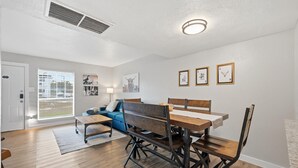 A dining area with a wooden table and chairs, a blue sofa, and a window with blinds. - Family, Business & Game-Day Getaway • Close to Arlington Attractions • Sleeps 8 (Arlington)