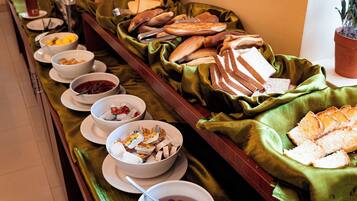 A buffet with various food items and bowls of fruit.