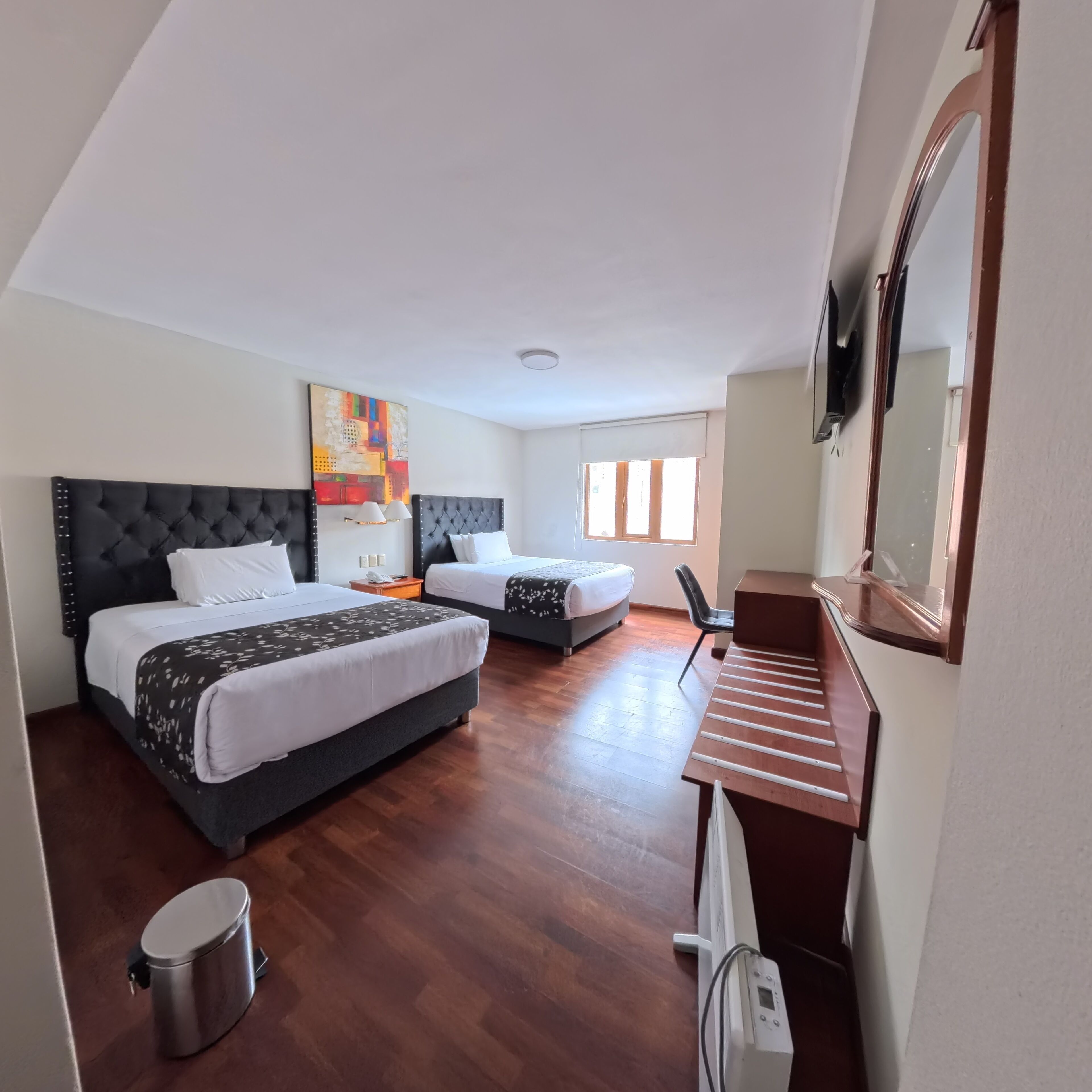 Habitación de hotel con dos camas, un escritorio, una silla, un cesto de basura y un espejo grande.