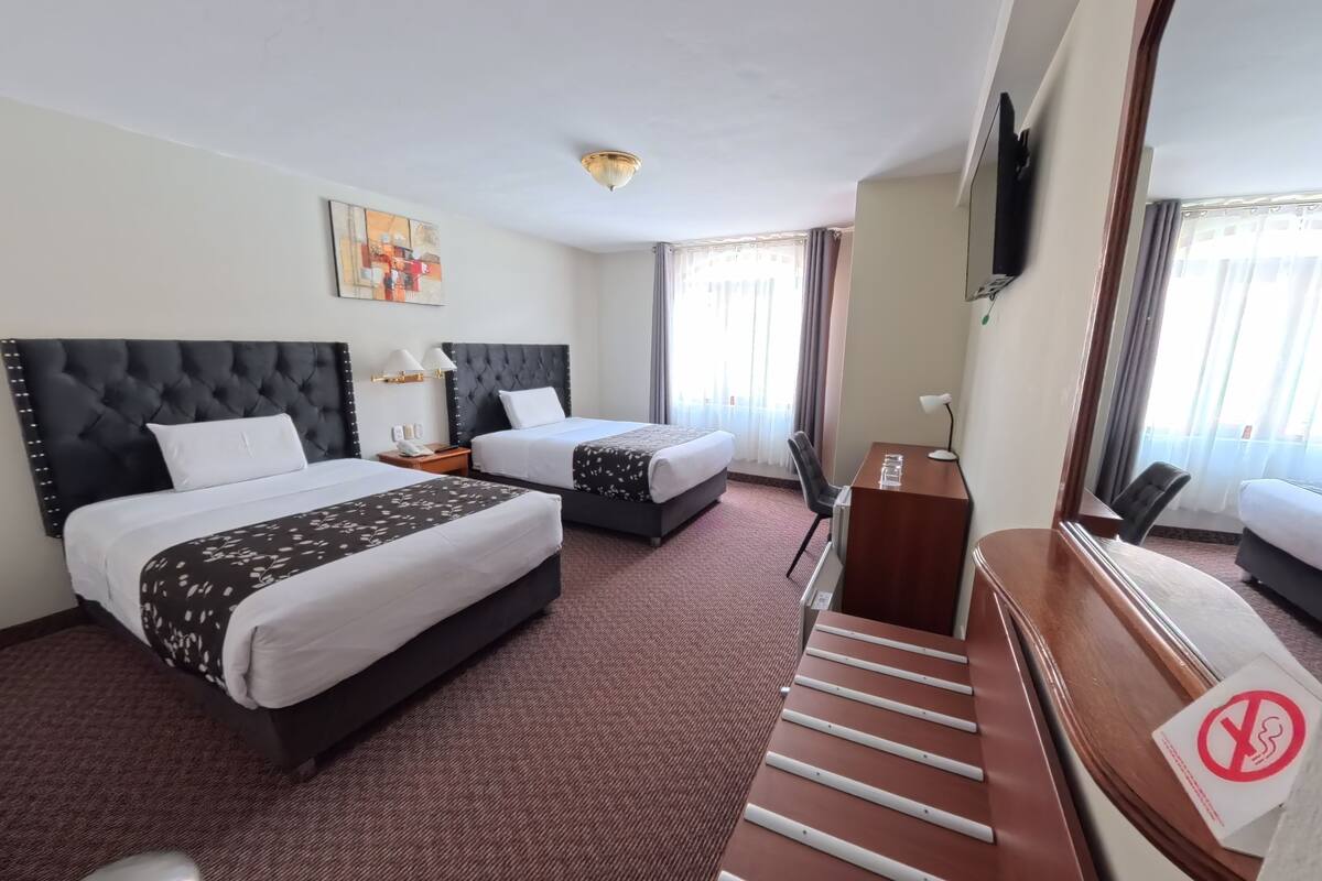 A hotel room with two beds, a desk, a chair, a TV, and a large mirror.