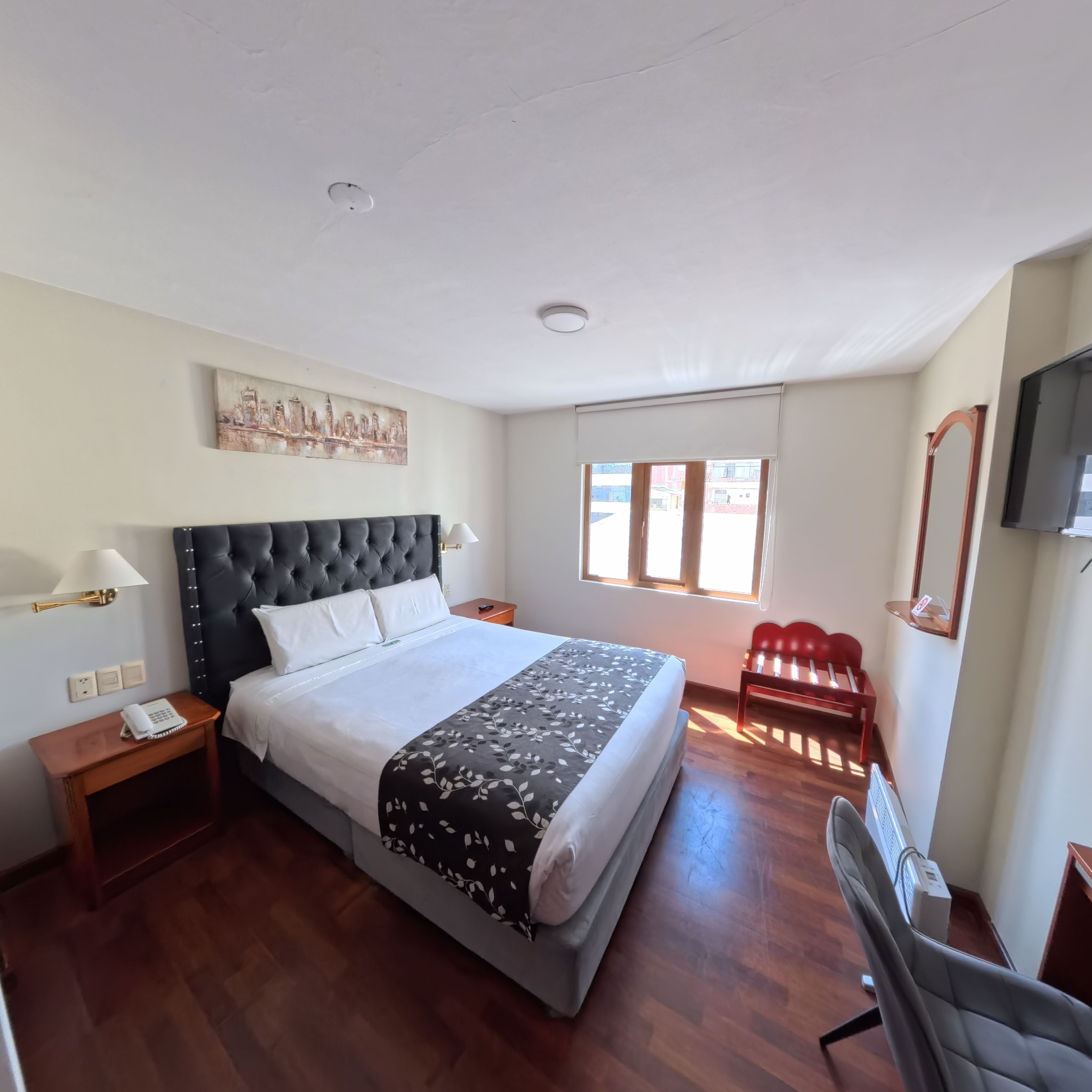 A hotel room with a large bed, a desk, a chair, a TV, and a window with blinds.