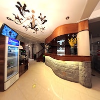 Un área de recepción con diseño moderno, que incluye un mostrador curvo, una araña y un refrigerador con bebidas.