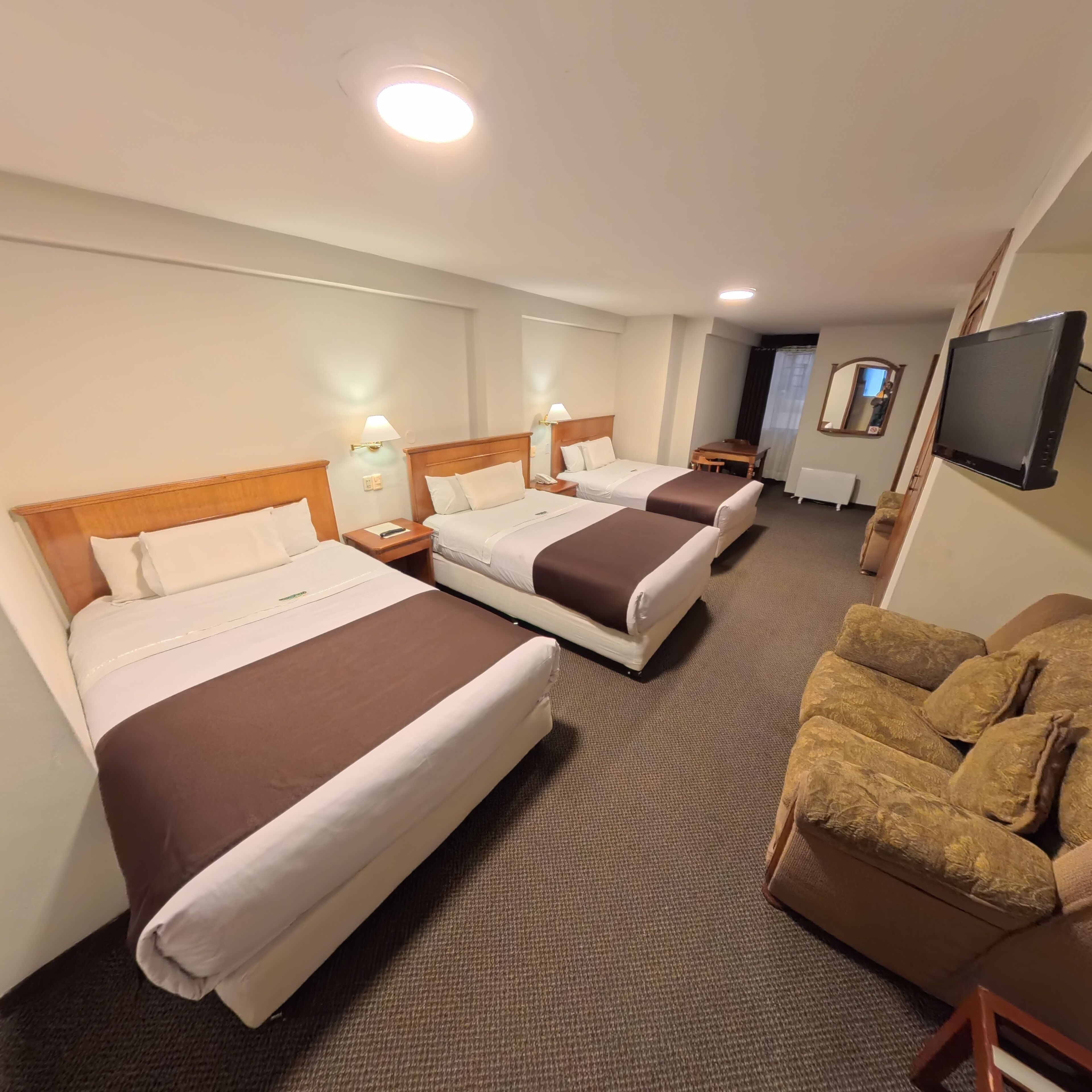 A hotel room with three beds, a TV, a desk, and a sofa.
