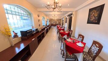 A long dining hall with red tablecloths, wooden chairs, and a chandelier.