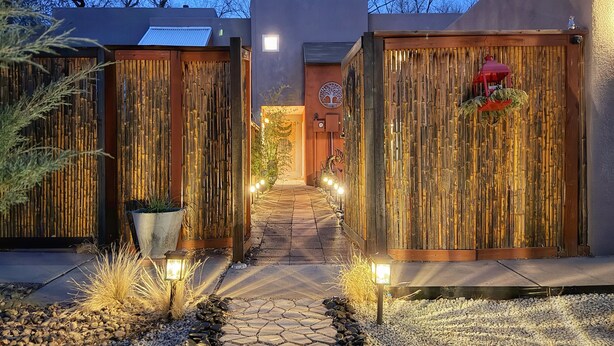 A pathway leading to a building with wooden fences and a tree symbol on the wall. - AirZen: Secure Gated 3BR Japandi Oasis w/ EV Garage, Trails & Views (Albuquerque)