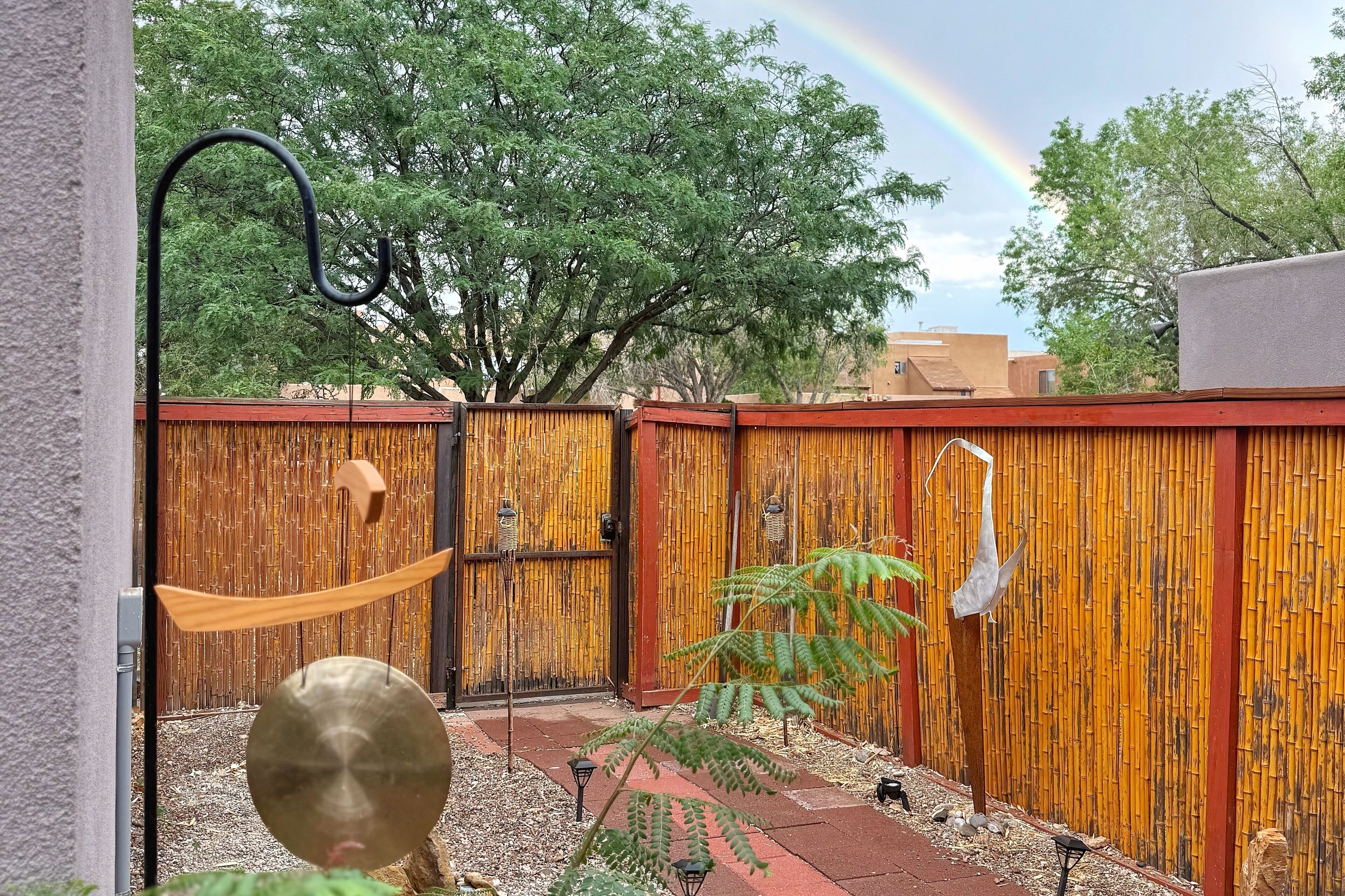A fenced backyard with a bamboo fence, a hanging bird sculpture, and a small garden area.