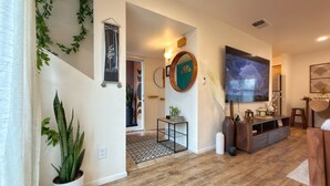 A modern living room with a large flat-screen TV, wooden flooring, and a mix of furniture including a sofa and a coffee table. - AirZen: Secure Gated 3BR Japandi Oasis w/ EV Garage, Trails & Views (Albuquerque)