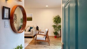 A living room with a sofa, a wooden chair, a round mirror, and a potted plant. - AirZen: Secure Gated 3BR Japandi Oasis w/ EV Garage, Trails & Views (Albuquerque)