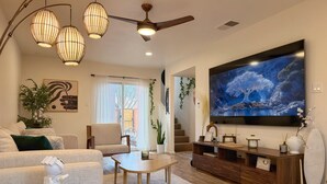 A spacious living room with a large flat-screen TV, comfortable seating, a ceiling fan, and a view of the outdoors through a sliding glass door. - AirZen: Secure Gated 3BR Japandi Oasis w/ EV Garage, Trails & Views (Albuquerque)
