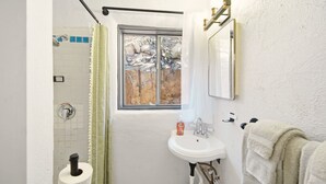 A bathroom with a shower, a sink, a window with a view of rocks, and a towel rack. - The Sunrise Studio - 1 Queen Bed (Truth or Consequences)