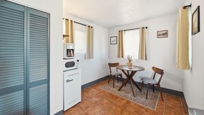 A compact kitchen with a refrigerator, microwave, and coffee maker. There is a small dining table with two chairs and a rug. - The Sunrise Studio - 1 Queen Bed (Truth or Consequences)