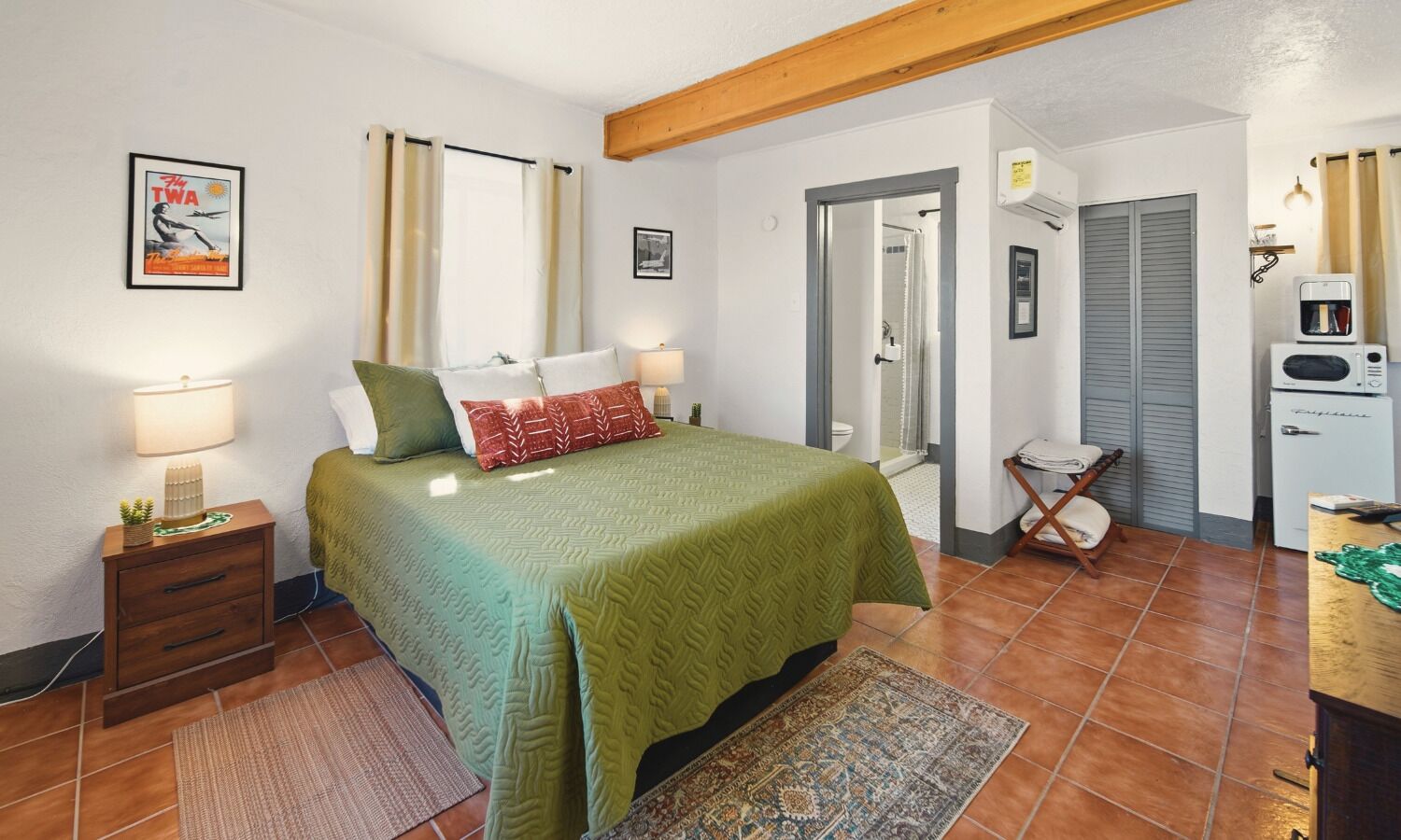 A bedroom with a bed, bedside tables, a nightstand, a mirror, a wardrobe, a radiator, and a small kitchenette. - The Sunrise Studio - 1 Queen Bed (Truth or Consequences)