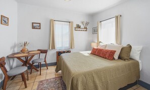 A bedroom with a bed, a desk, two chairs, a rug, and a window with curtains.